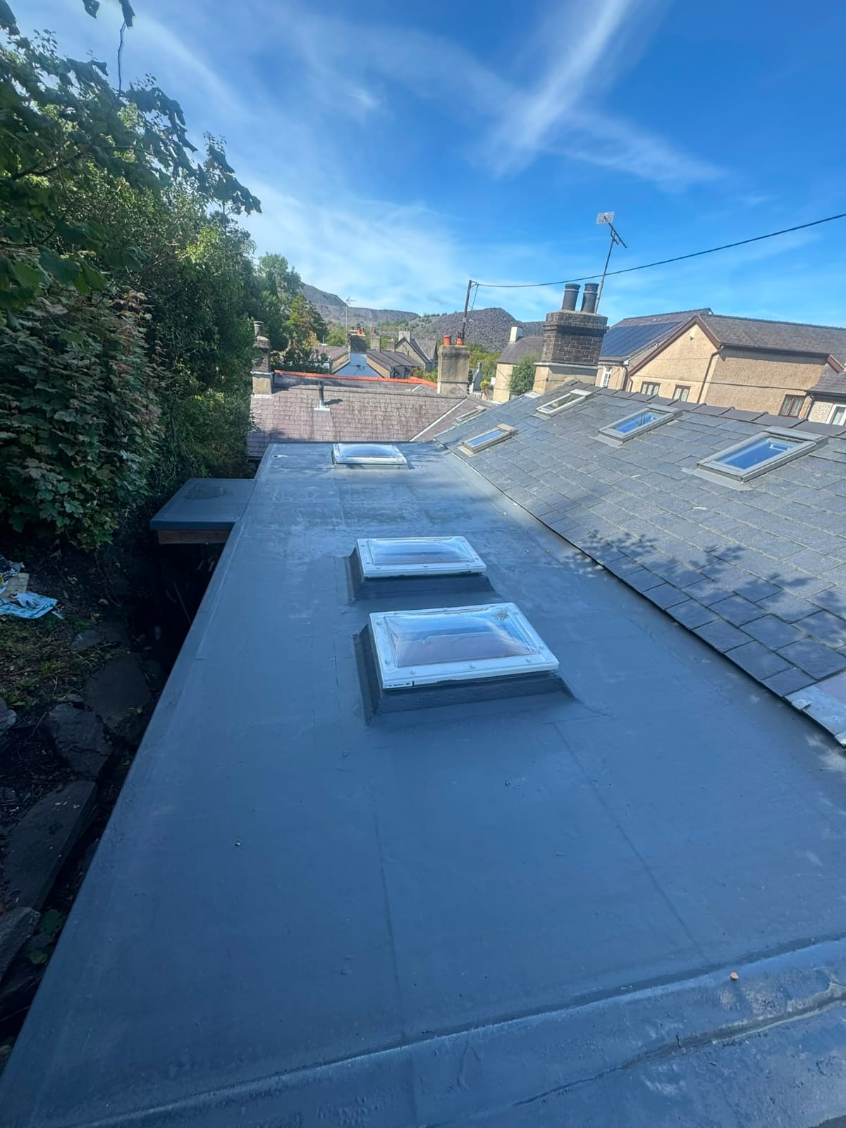 Fibreglass flat roof with three new rooflights above a slate-roofed terrace in North Wales