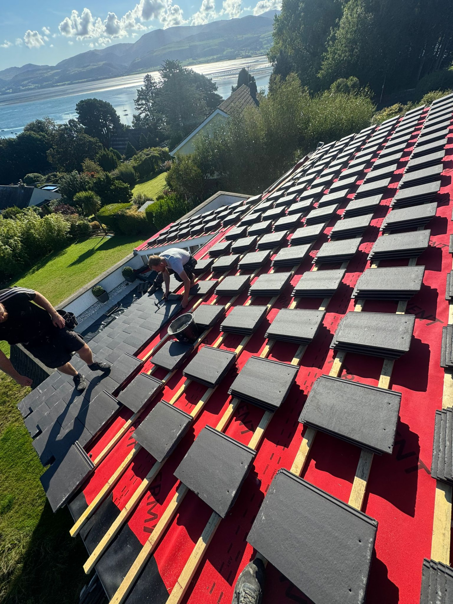 Roofers laying new Welsh slate tiles on a re-roof in North Wales